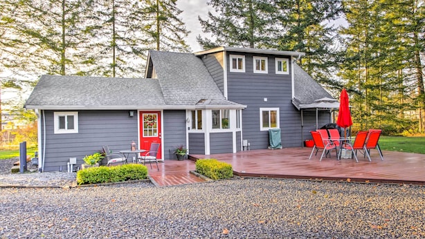 A two-story house with a deck, a red door, and a patio with red chairs and a table. - Peacock Hill Retreat on 1 Acre, 1 Mi to Harbor (Gig Harbor)