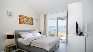 A bedroom with a bed, a nightstand, a TV, and a view of the sea. - Stunning Villa Avalon for 9 Pool 2 Mins to Beach (Okrug)