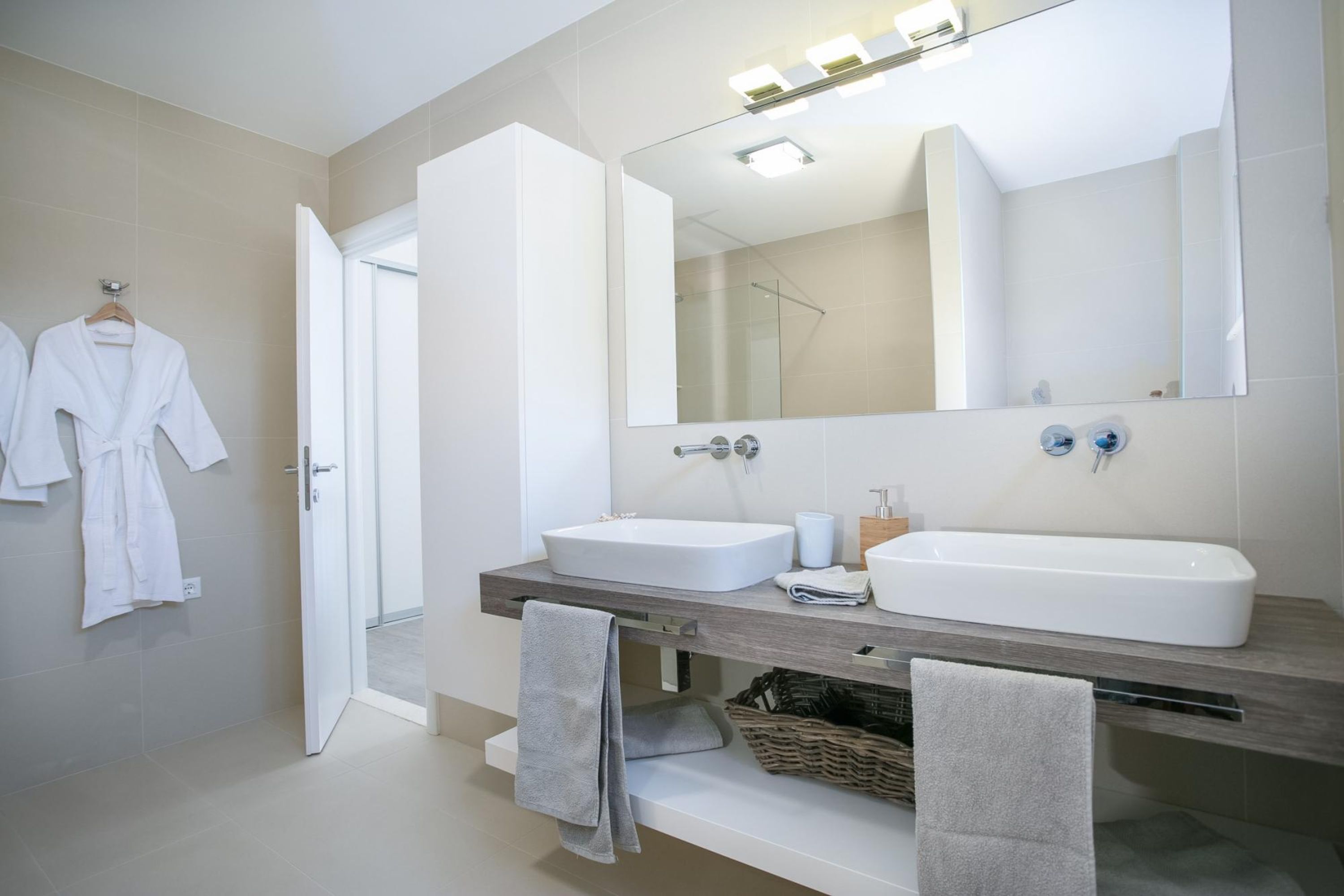 A modern bathroom with two sinks, a large mirror, and a towel rack.