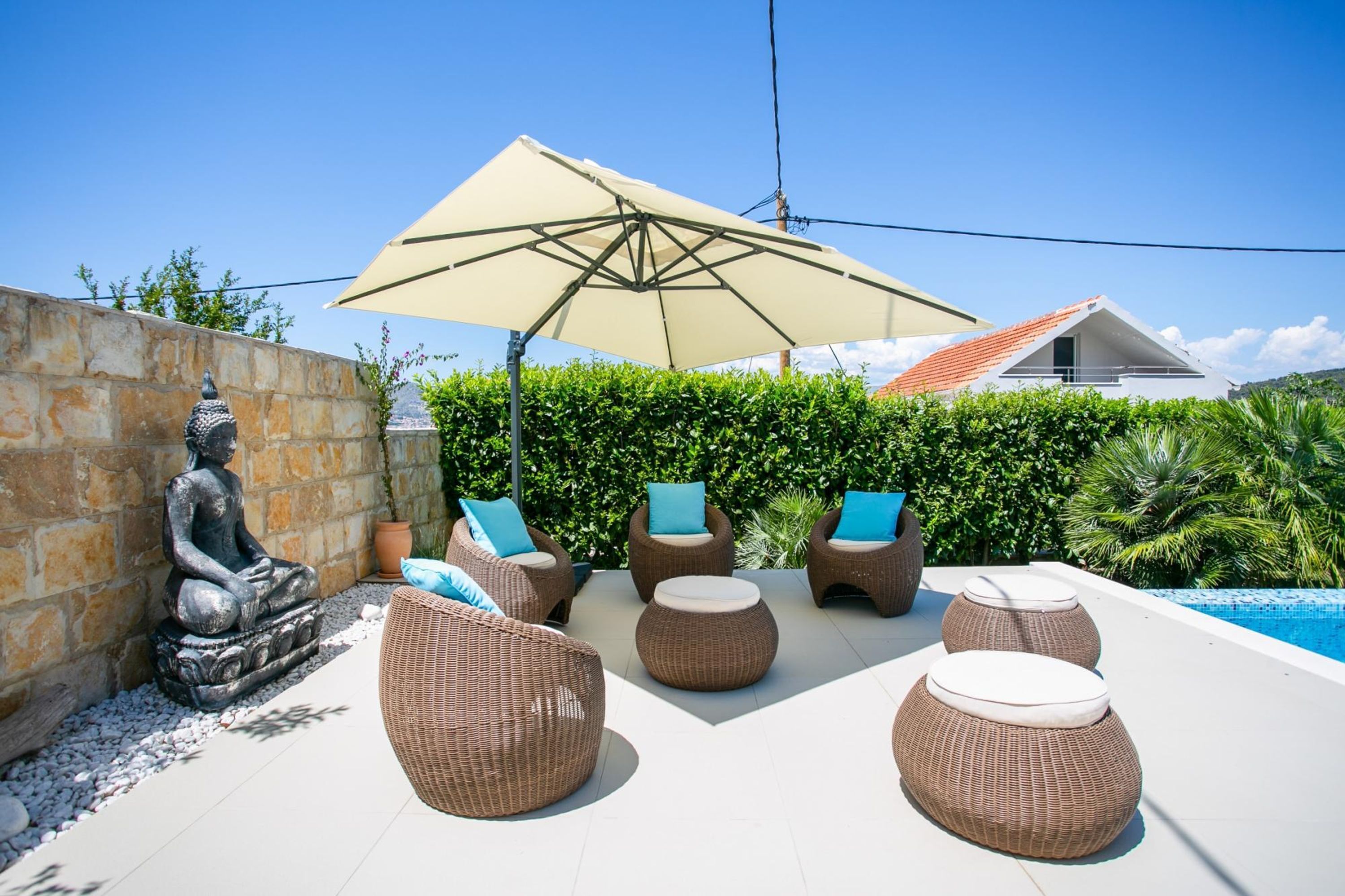 A patio with wicker furniture, a Buddha statue, and a swimming pool.