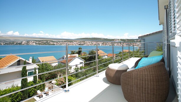 A balcony with wicker furniture, a view of the sea, and buildings in the background. - Stunning Villa Avalon for 9 Pool 2 Mins to Beach (Okrug)
