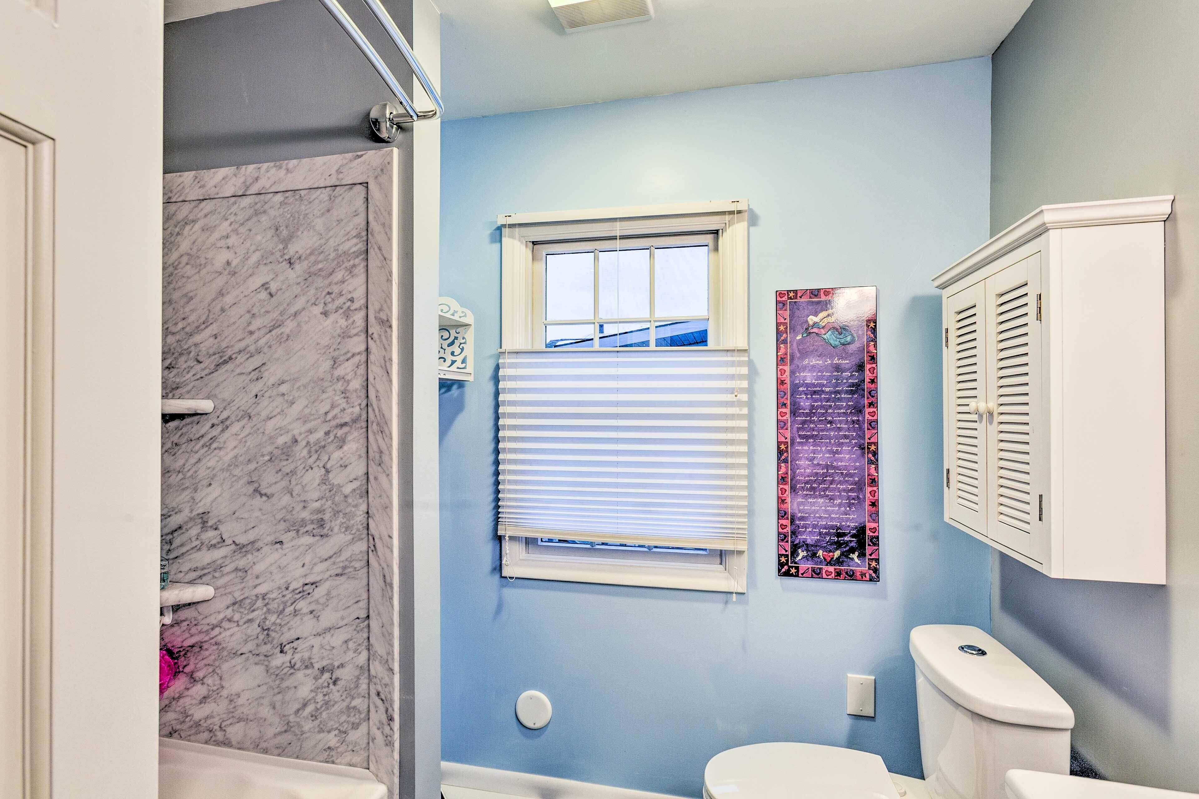Een badkamer met een douche van marmer, een toilet en een raam met zonwering.