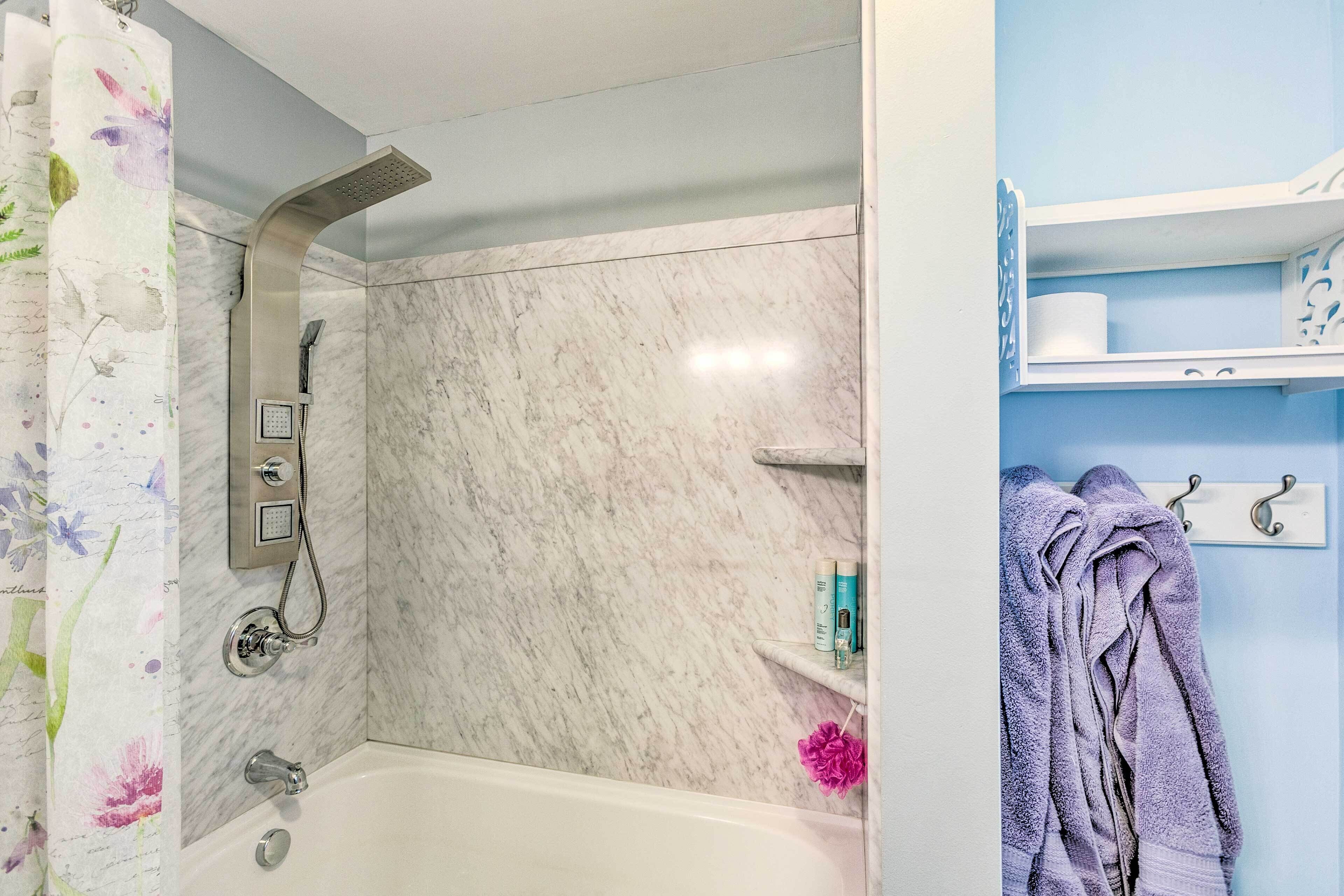 A bathroom with a bathtub, a shower, and a toilet. There are towels and toiletries on a shelf.