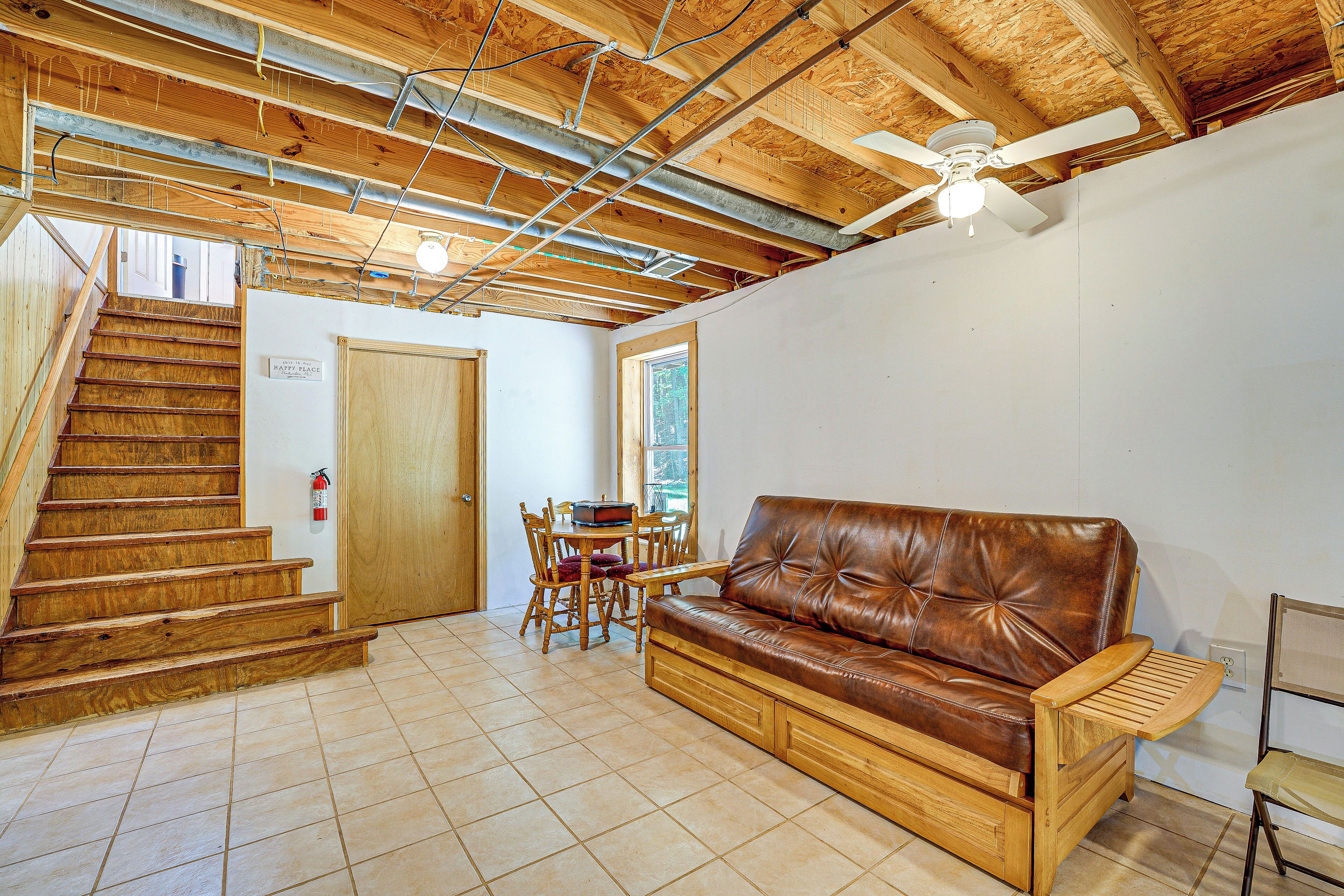 A wooden staircase leading to a door, a brown leather sofa, a dining table with chairs, and a ceiling fan.