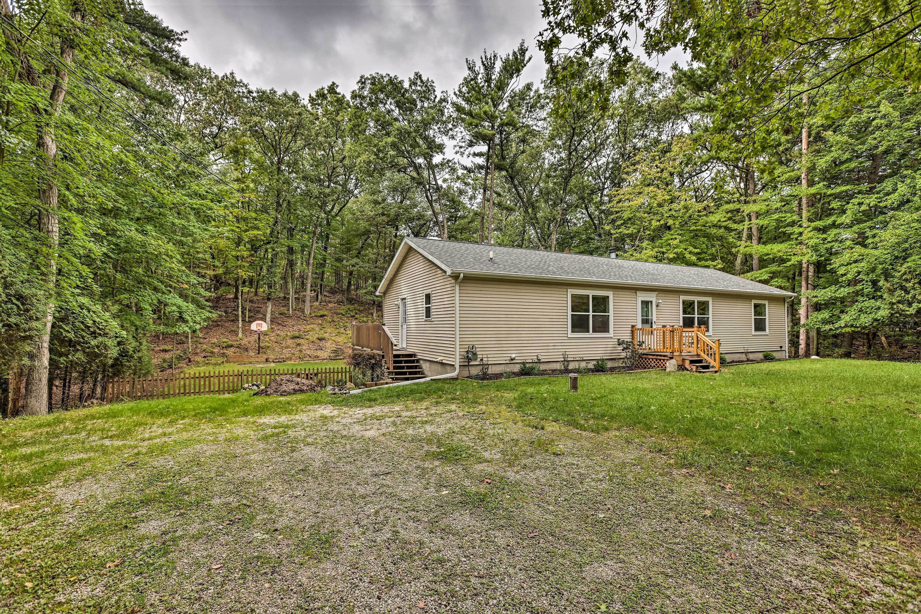 A single-story house with a front deck, surrounded by a forested area.