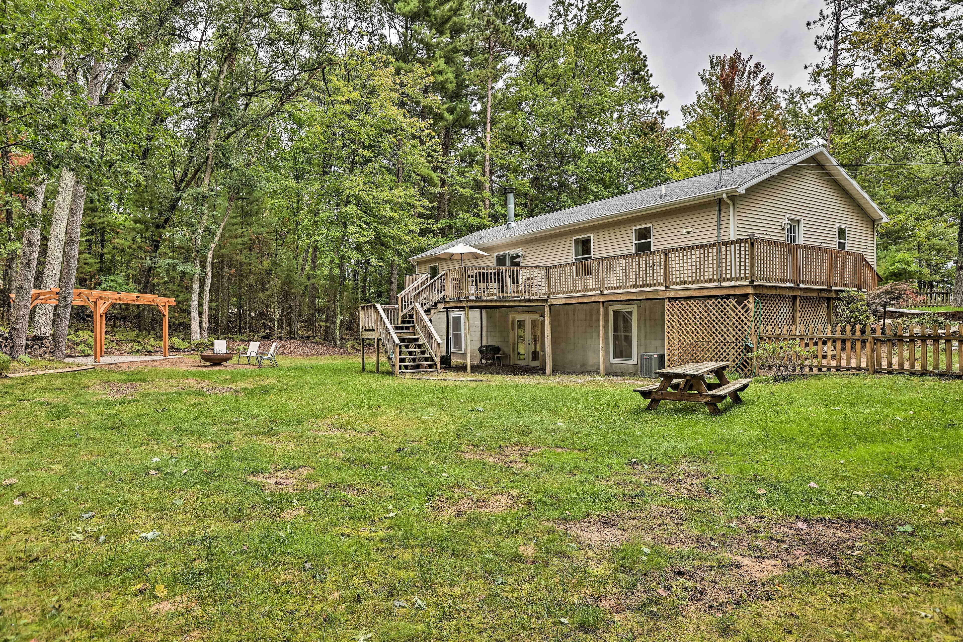 A two-story house with a deck, a covered patio, and a picnic table in a wooded area.