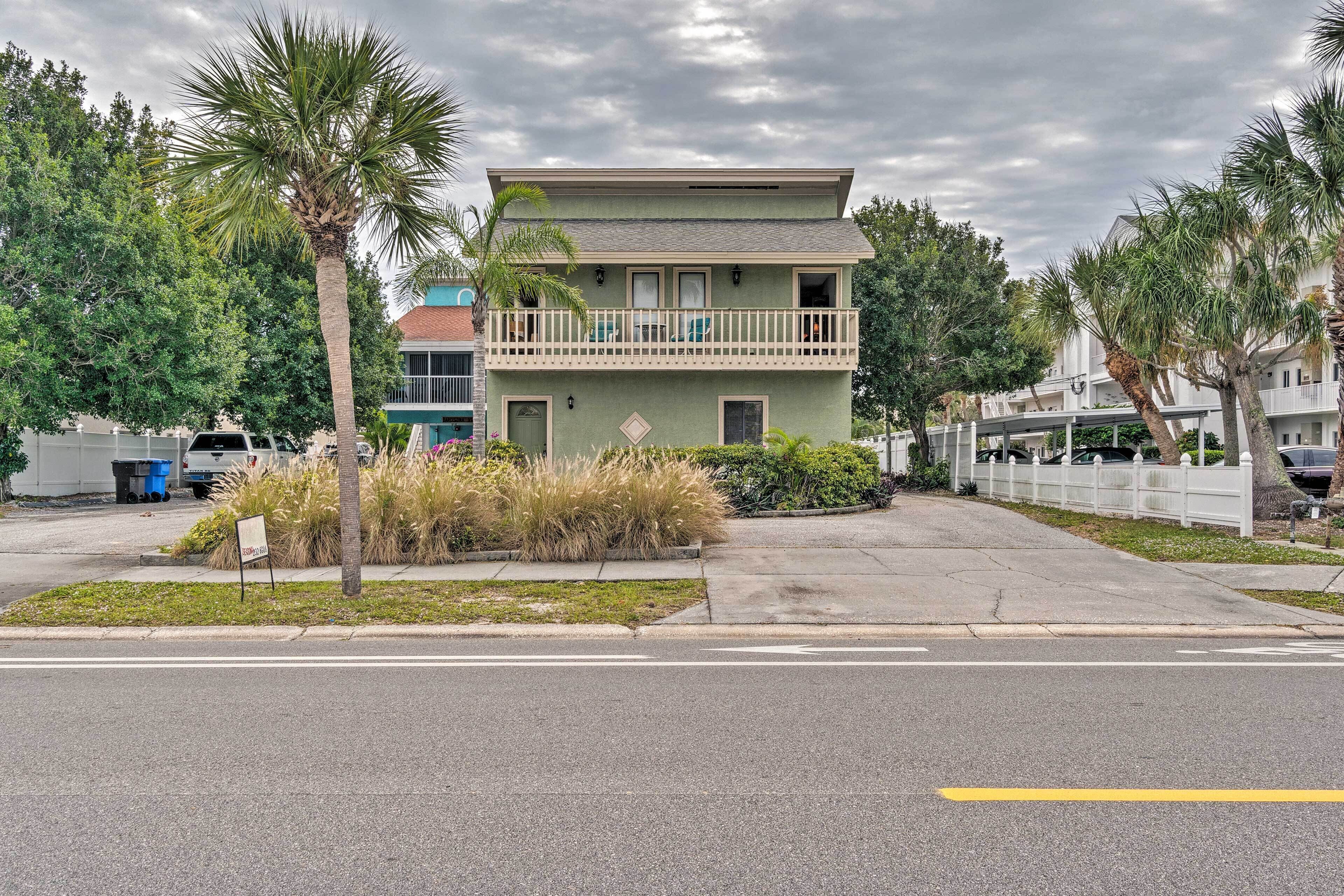 A two-story building with a balcony, surrounded by palm trees and a grassy area.