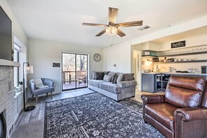 A spacious living room with a fireplace, a ceiling fan, and a coffee station.