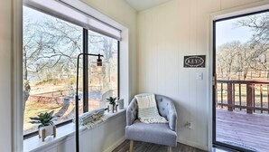 Een kamer met uitzicht op een houten terras en bomen, een stoel met een plaid, een radiator, en een bordje met de tekst 'KEYS'.