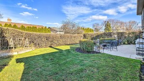 A well-maintained backyard with a patio area, outdoor furniture, and a hedge. - Elegant Mount Prospect Home w/ Fire Pit! (Mount Prospect)