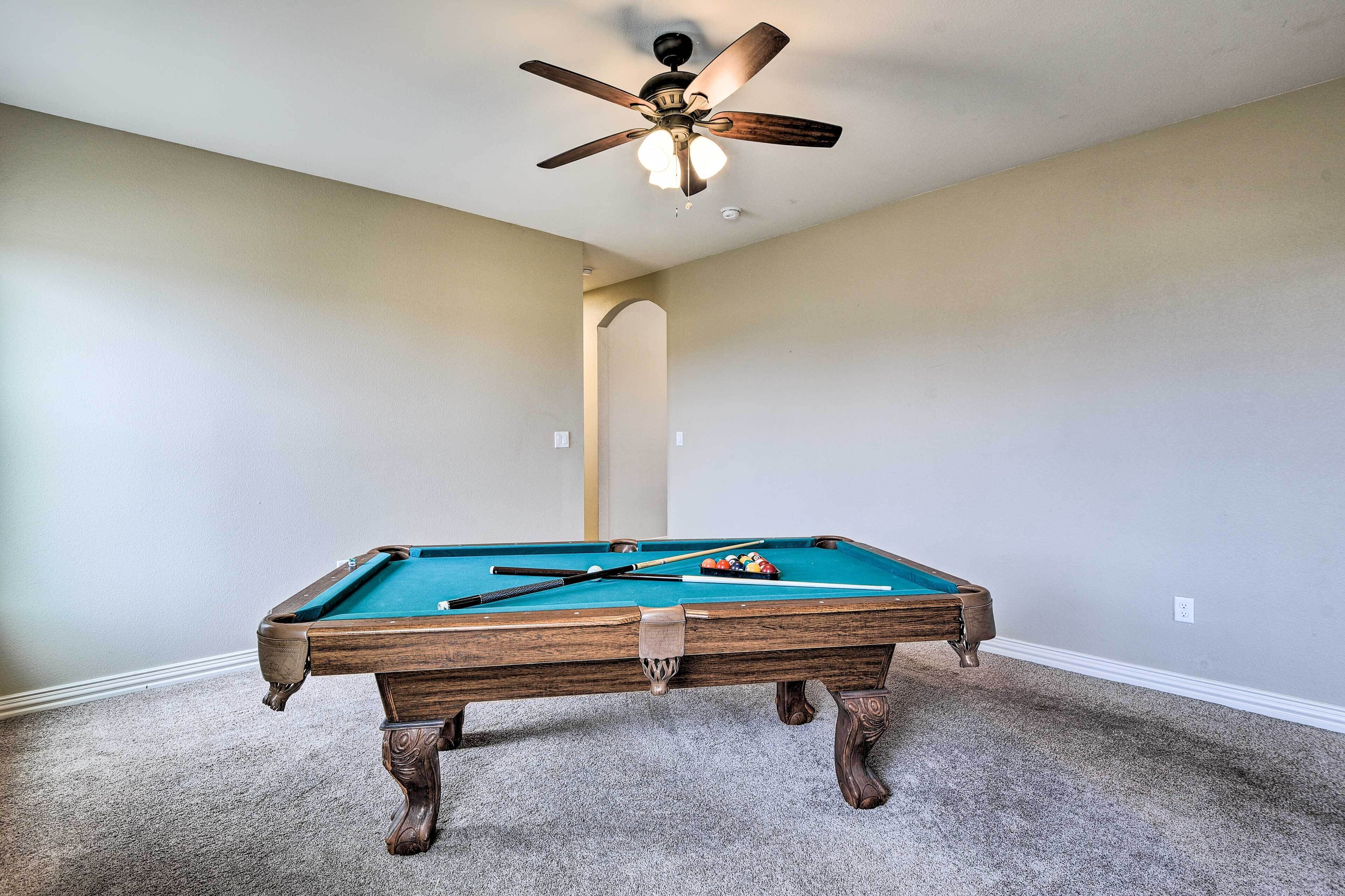 A pool table in a room with a ceiling fan and carpeted floor.