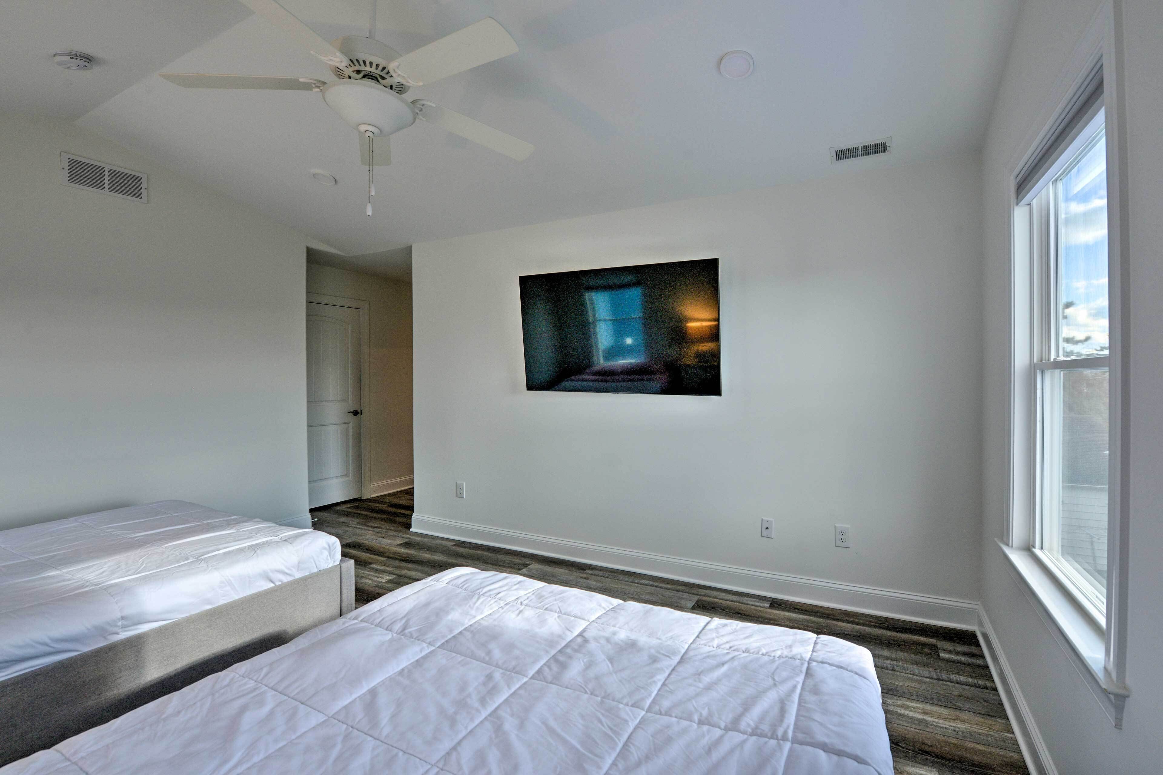 A bedroom with two beds, a ceiling fan, a large window, and a painting on the wall.