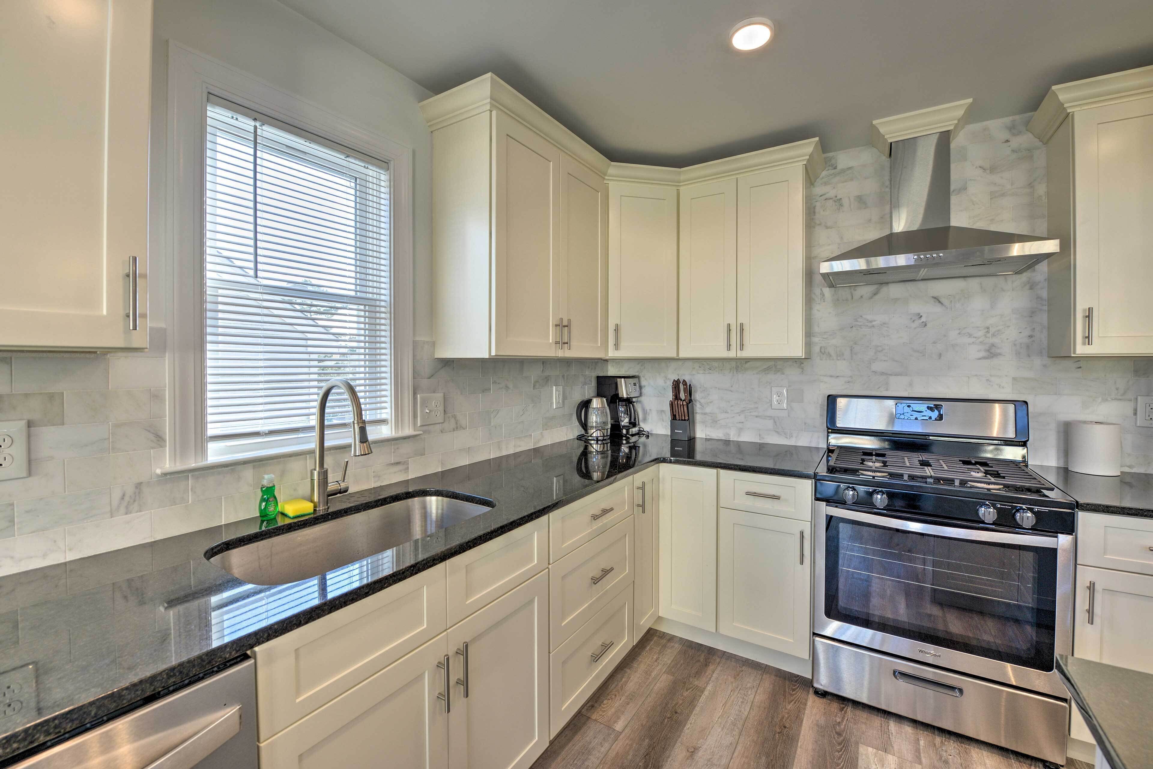 A modern kitchen with white cabinets, a stainless steel stove, and a large window with blinds.