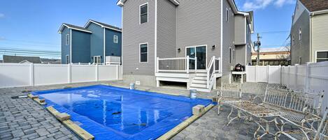 A residential area with a swimming pool, a covered patio, and a white metal bench.