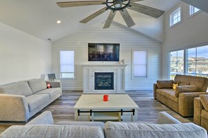 Amplia sala de estar con ventilador de techo alto, chimenea y ventanas grandes que ofrecen vistas al exterior.