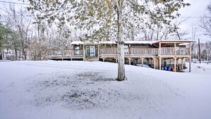 Una cabaña con terraza y porche cubierto, rodeada de nieve y árboles.
