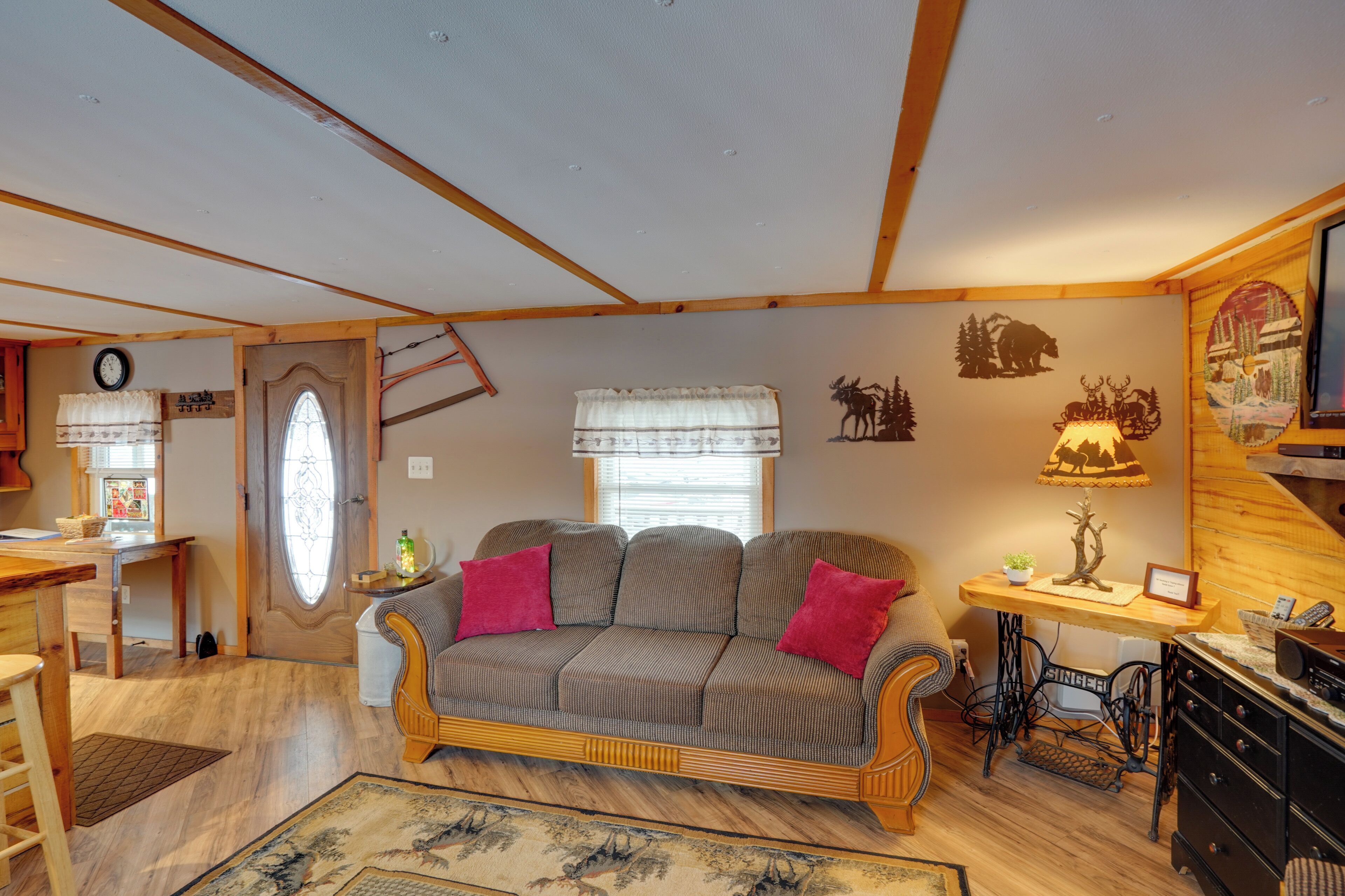A cozy living room with a sofa, a dining table, a sewing machine, and a window with curtains.