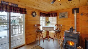Interior acogedor de una cabaña con un estufa de leña, dos sillones, una mesa y un letrero que dice 'Bootleggers Tavern'.