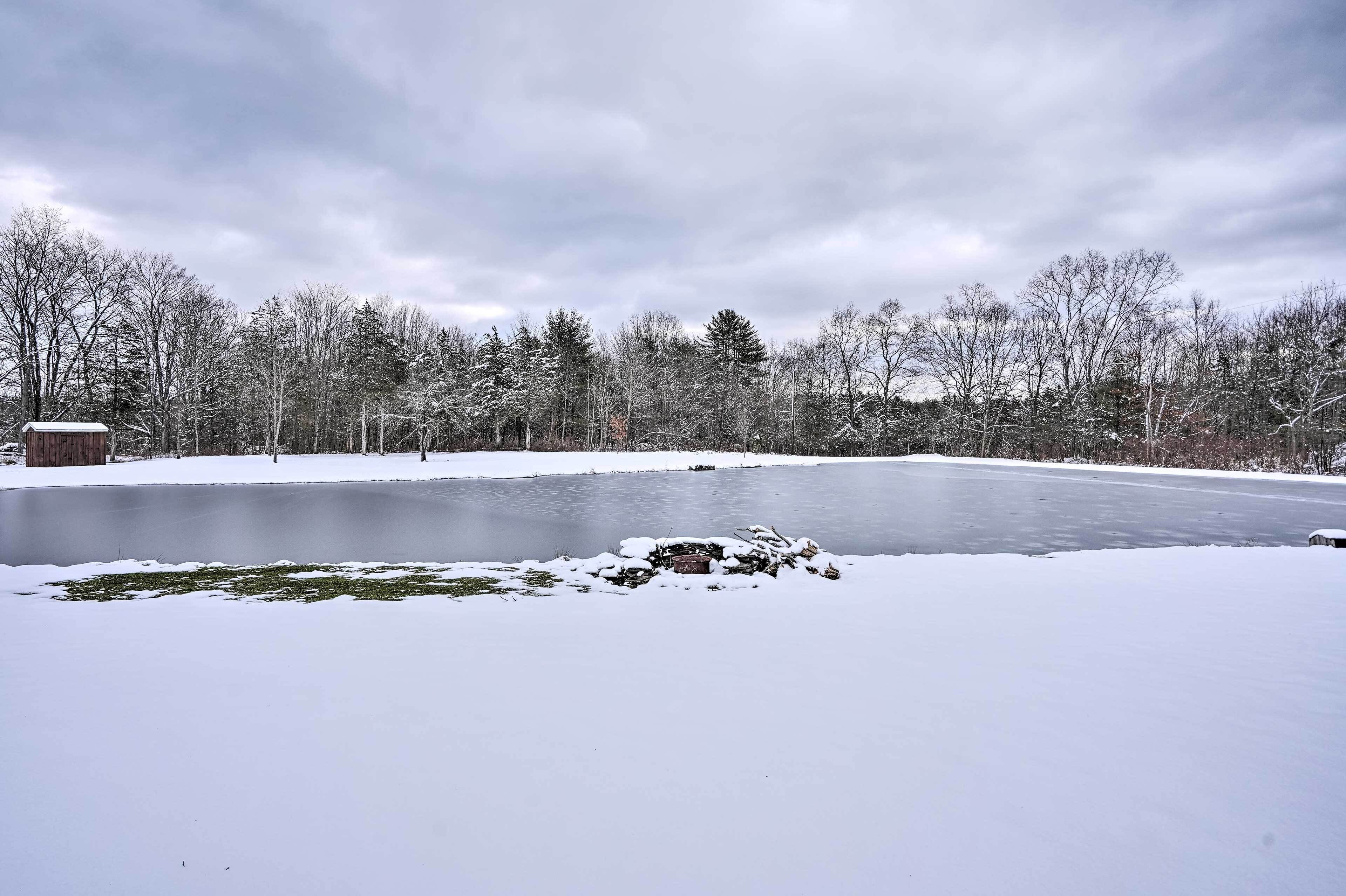 A snow-covered landscape with a frozen lake, trees, and a small wooden structure.