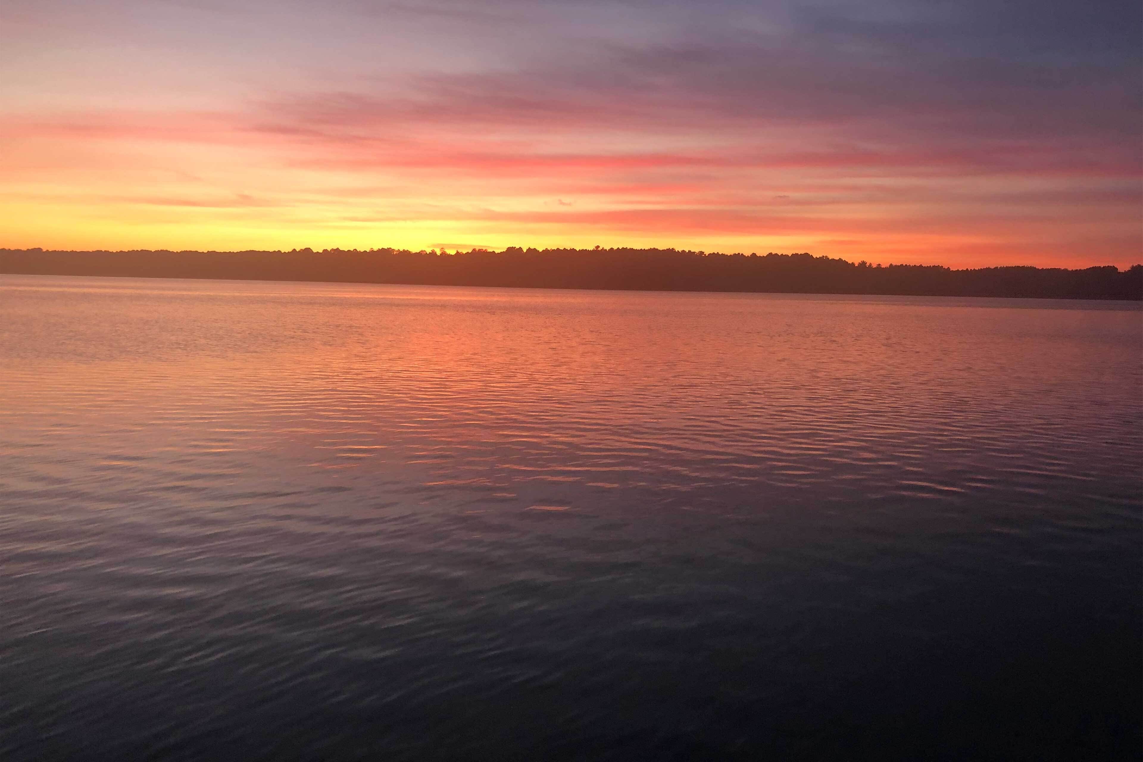 A calm lake at sunset with a forested shoreline.