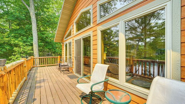 A wooden deck with a glass door leading to a covered outdoor area, furnished with a chair and a table. - Four-season Lake Cabin w/ Canoe & Paddle Boat! (Gordon)