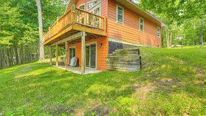 A two-story wooden house with a balcony, surrounded by lush greenery. - Four-season Lake Cabin w/ Canoe & Paddle Boat! (Gordon)