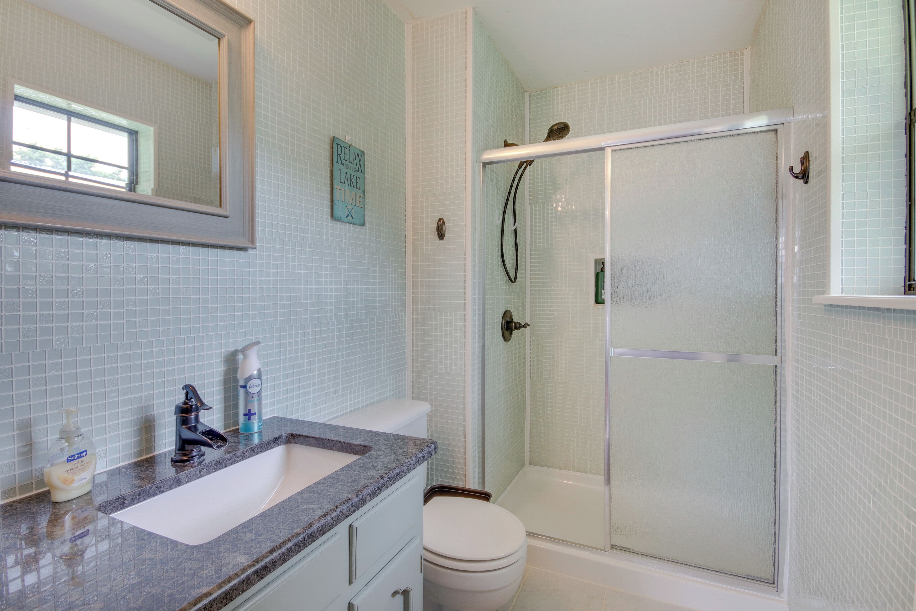Un bagno con lavandino bianco, uno specchio, un water e una cabina doccia in vetro.