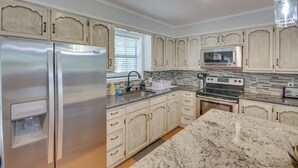 A kitchen with a stainless steel refrigerator, a microwave, a stove, and a sink. - Yard + 15' Boat Slip: Waterfront Grove Getaway (Grove)