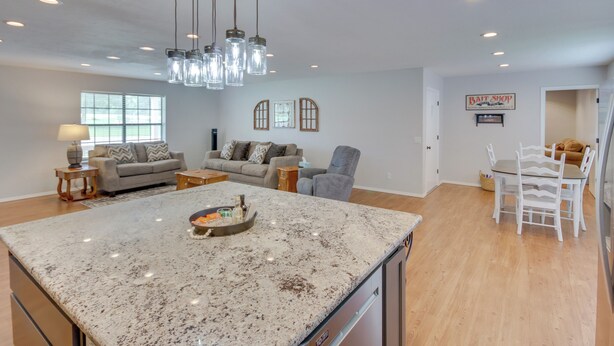 A spacious kitchen with granite countertops, a dining area with white chairs, a gray sofa, and a chandelier. - Yard + 15' Boat Slip: Waterfront Grove Getaway (Grove)