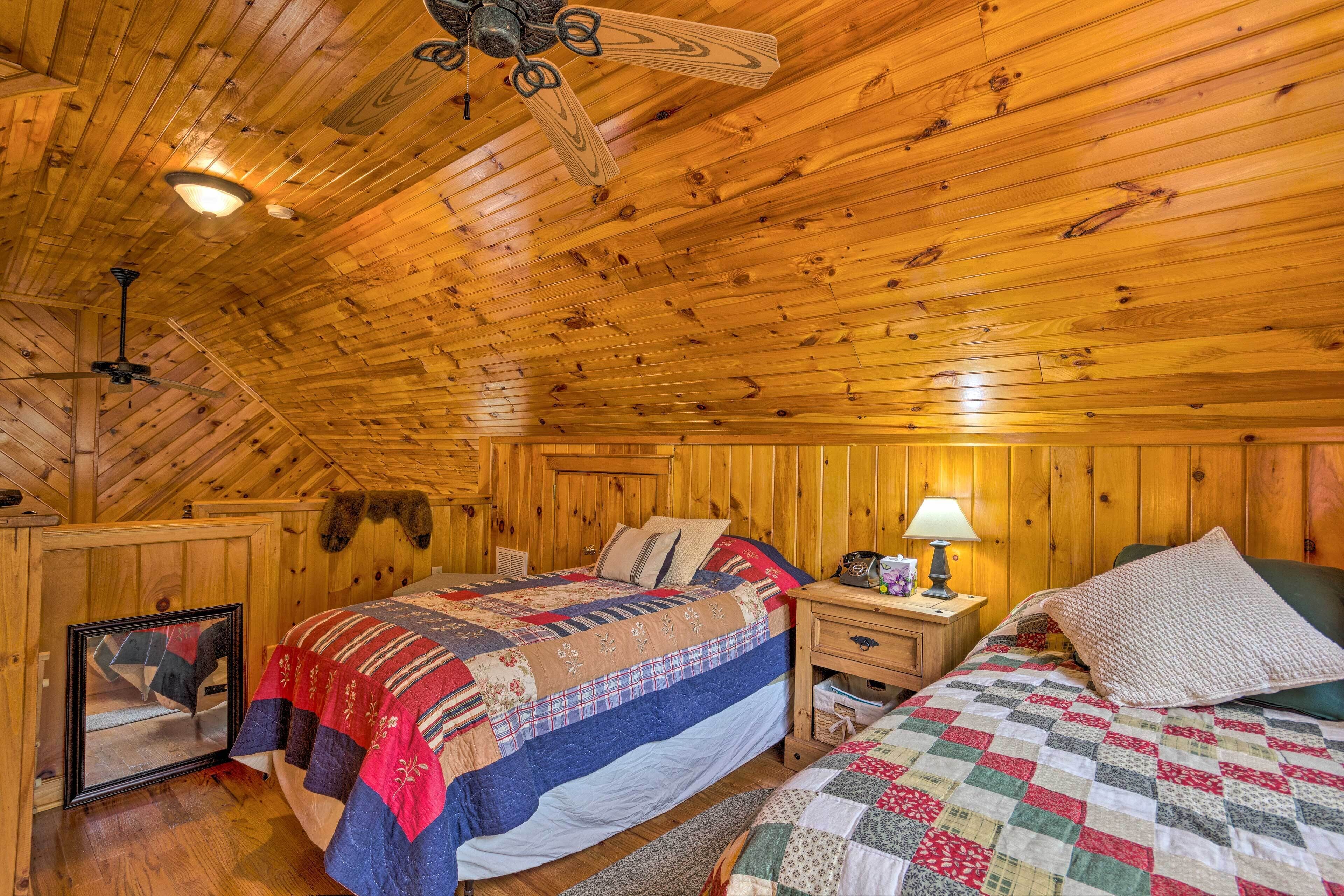 Ein gemütliches Schlafzimmer in einer Holzhütte, mit Holzwänden und -decke, einem Bett mit Patchworkdecke, einem Nachttisch mit Lampe und einem gerahmten Bild an der Wand.