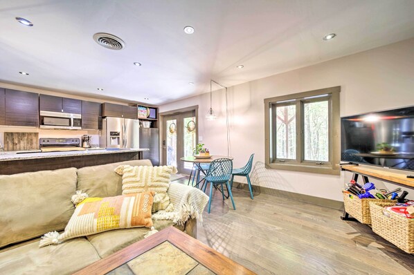 A modern kitchen with built-in appliances, a dining area with blue chairs, and a large TV. - Chic Brevard Cabin - Nature, Trails, & Water! (Brevard)