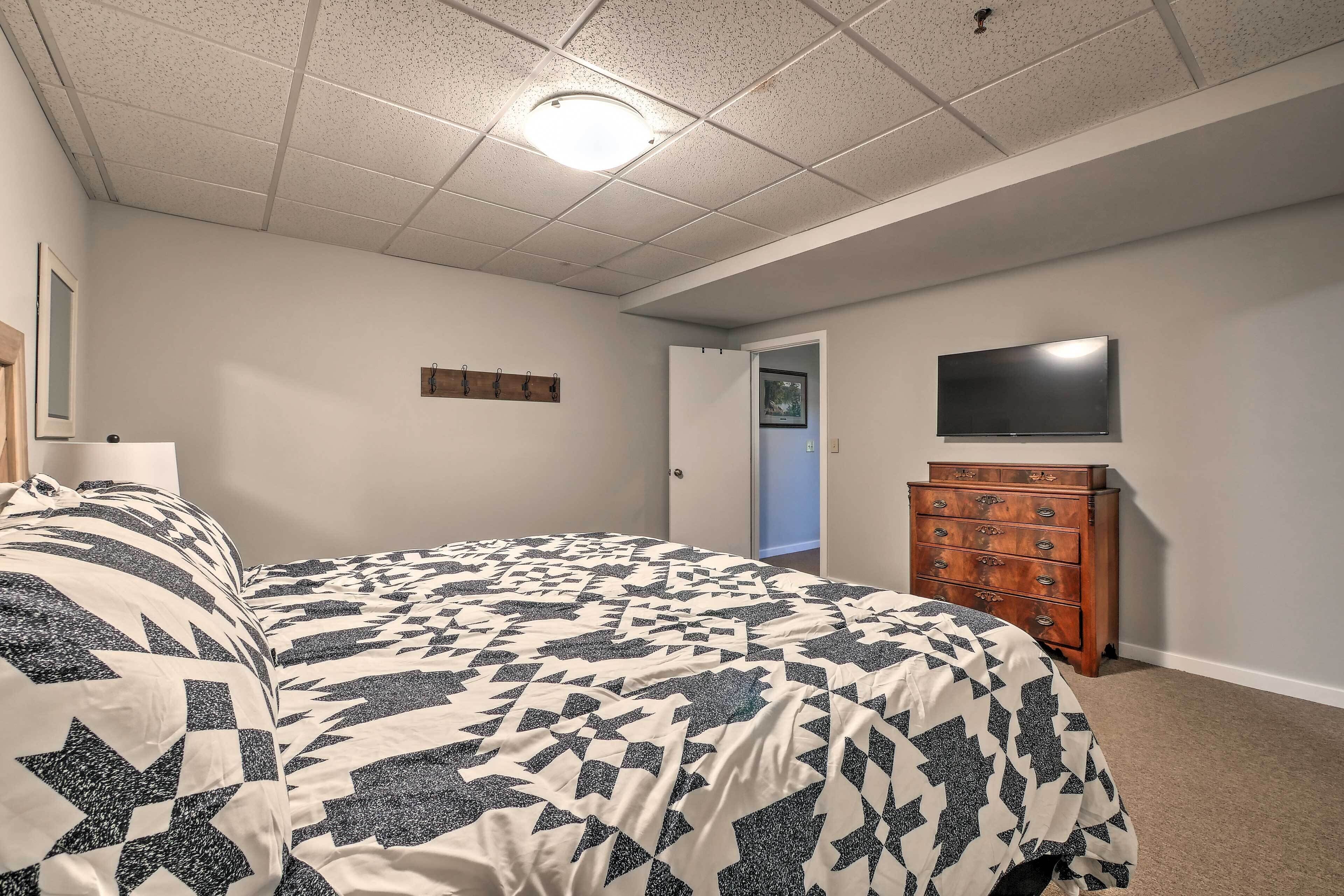 A bedroom with a bed, dresser, TV, and a door leading to another room.