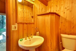 Une salle de bain aux murs lambrissés, avec un lavabo blanc, un miroir et des toilettes.
