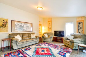 Un salon avec un canapé, deux fauteuils, un téléviseur et un tapis à motifs.