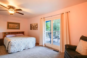 A bedroom with a bed, a ceiling fan, a sliding glass door to a balcony, and a chair.