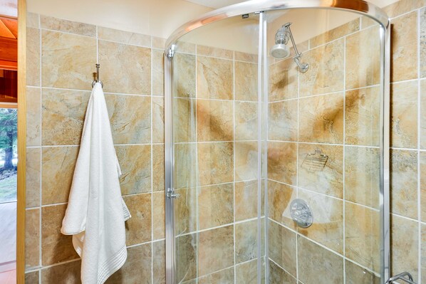 Une douche avec une porte en verre, des carreaux de couleur beige et une serviette blanche accrochée au mur.