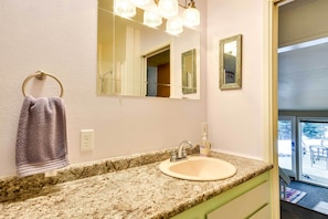 A bathroom with a granite countertop, a sink, a towel ring, a mirror, and a door leading to a balcony.