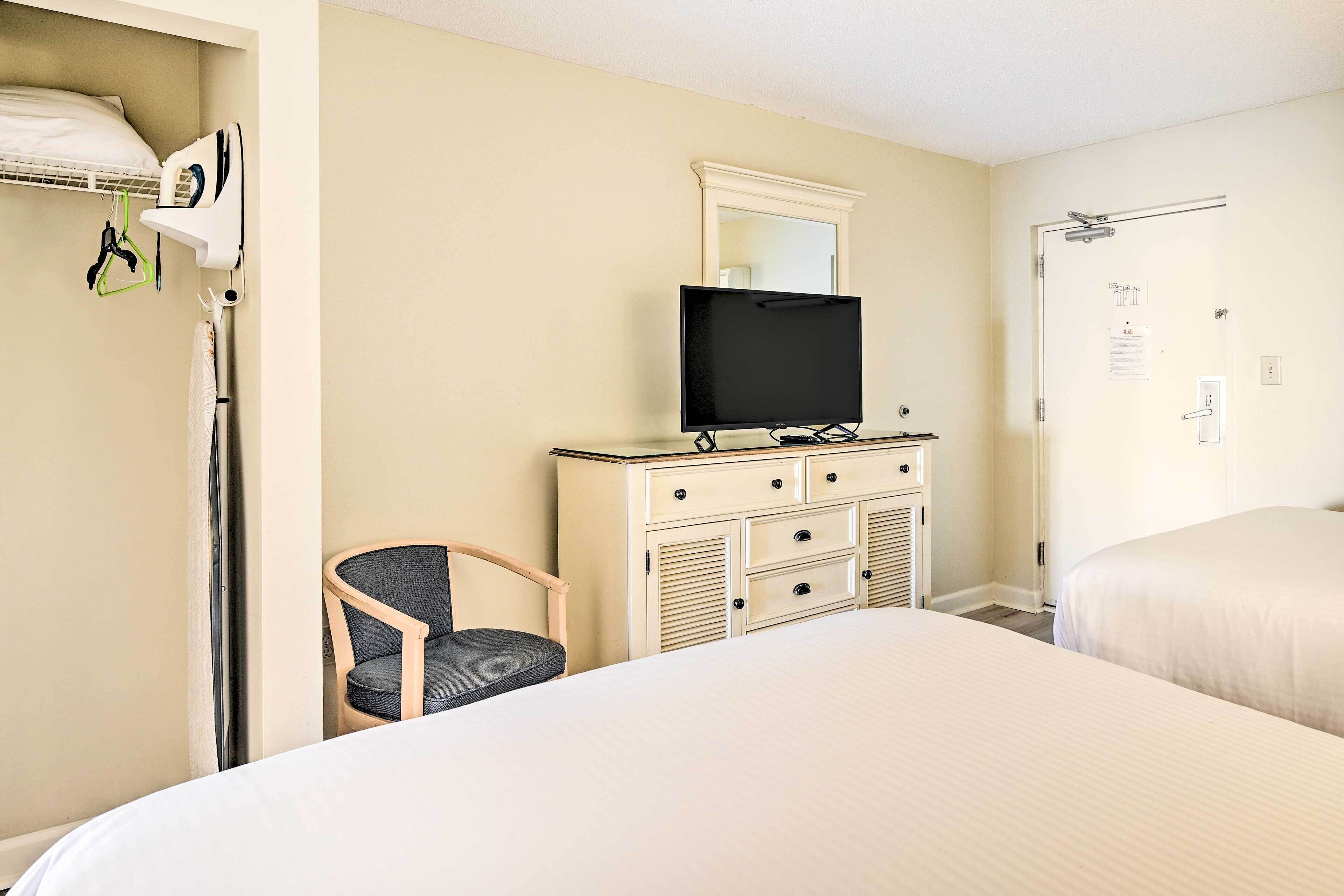 Hotelkamer met twee bedden, een televisie op een dressoir, een stoel en een deur met een spiegel erboven.