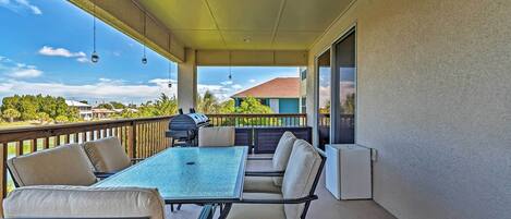 A covered patio with a table and chairs, a grill, and a view of a house in the background.