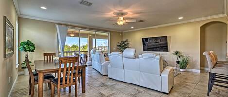 A spacious living room with a dining area, a ceiling fan, and a large window offering a view.