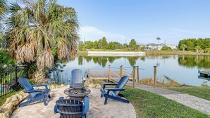 Une terrasse extérieure avec des fauteuils Adirondack, un foyer et une vue sur un lac.