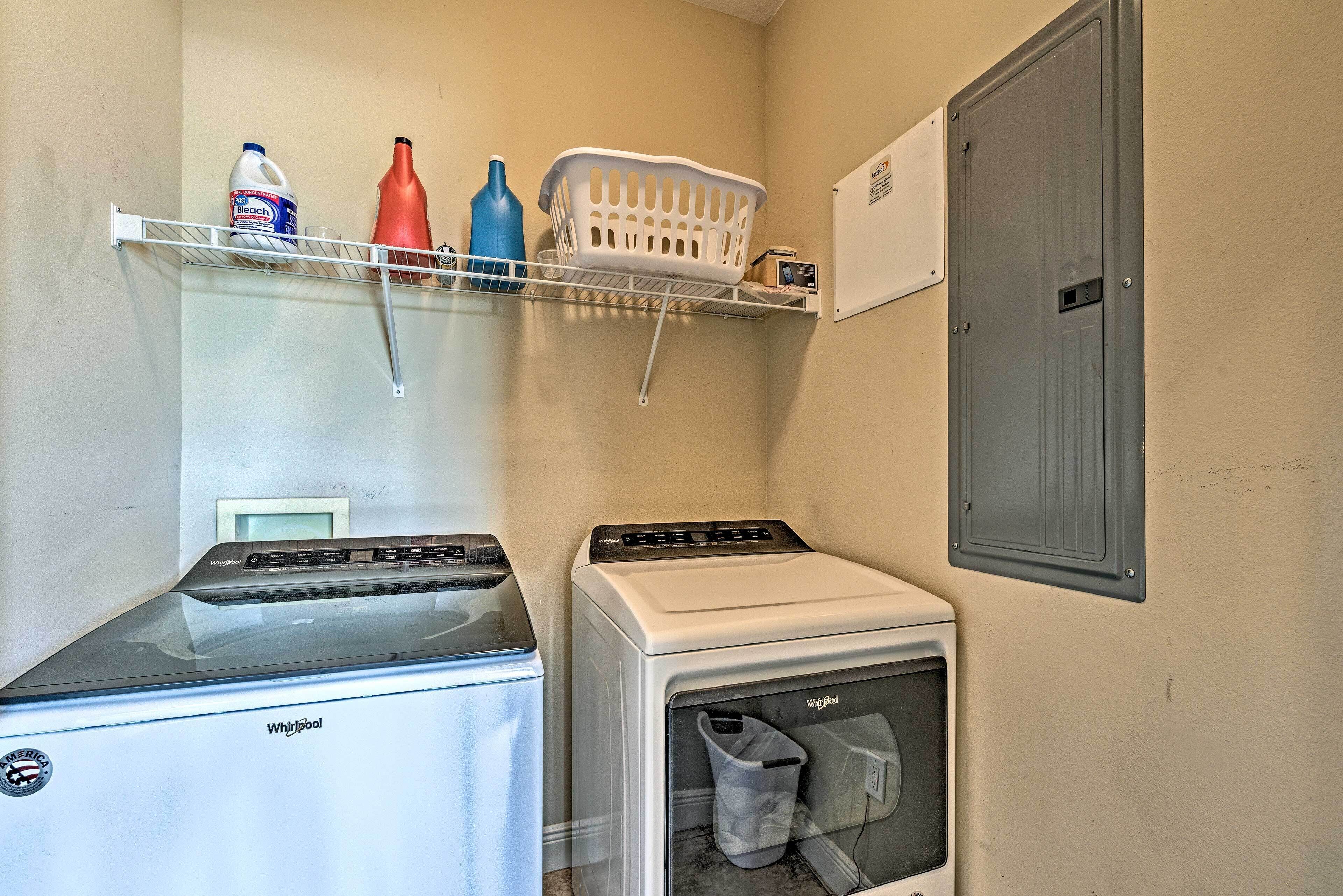 Un lavadero con dos lavadoras Whirlpool, un estante con productos de limpieza y un armario de servicios gris.