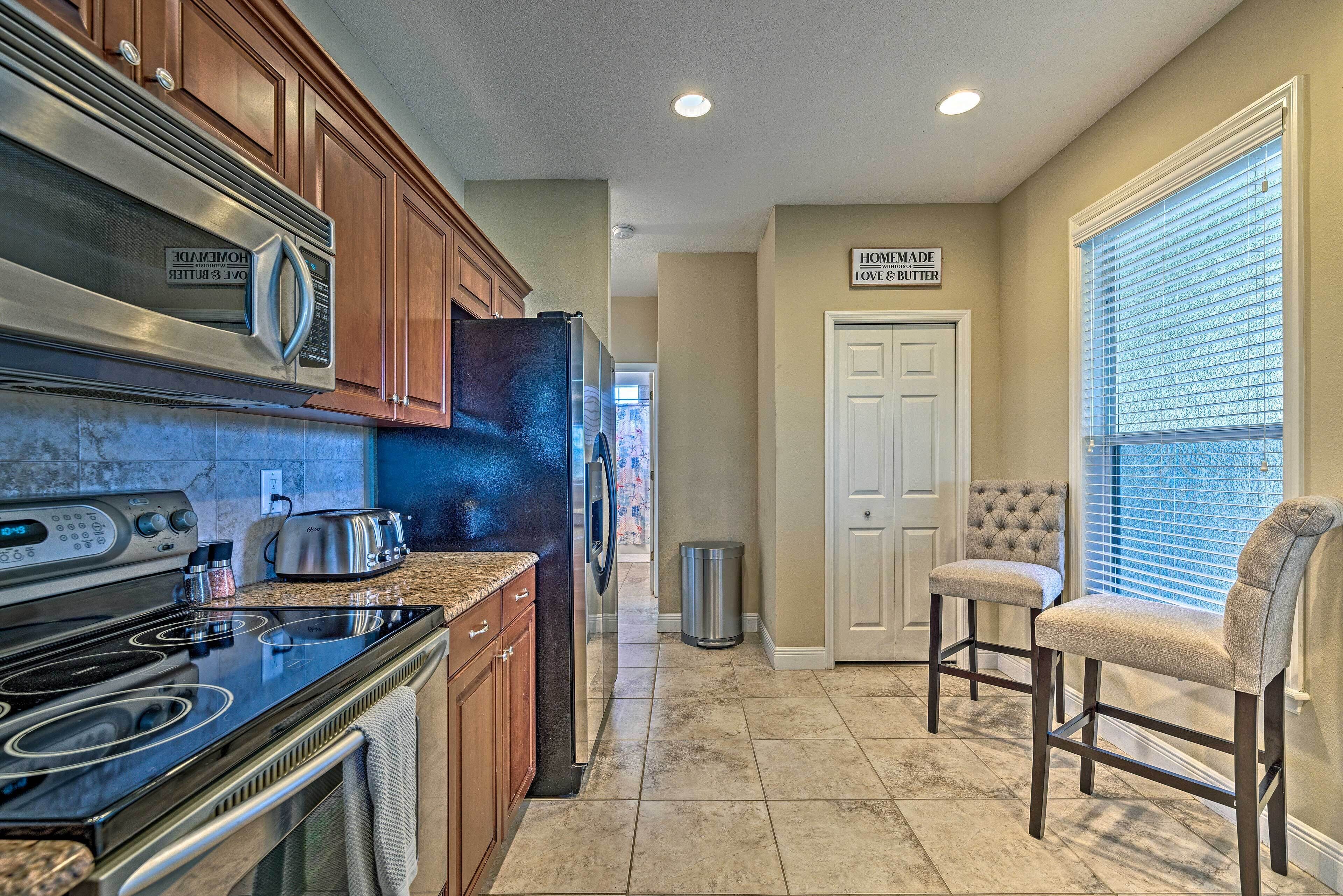 A kitchen with a stove, oven, microwave, and toaster. There is a trash can and a door leading to another room.