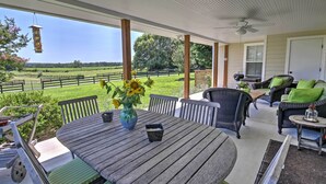 A covered patio with a table and chairs, a hanging lantern, and a view of a green field.