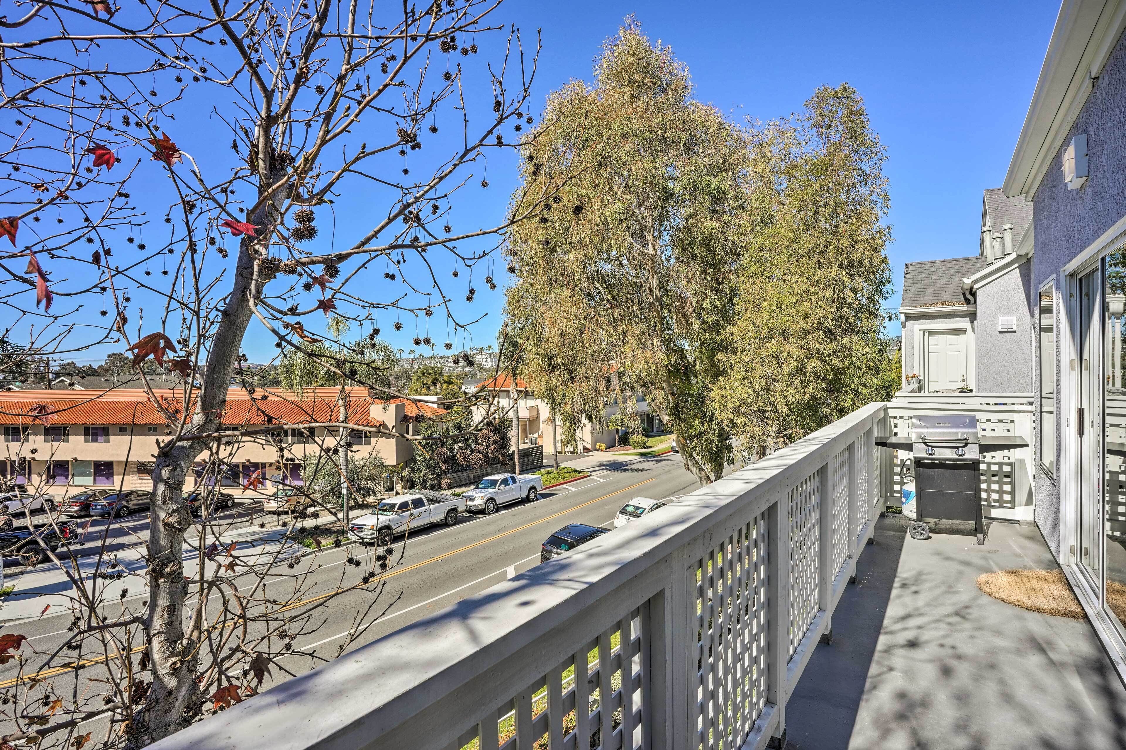 A balcony with a view of a street, a tree, and a building with a barbecue grill.