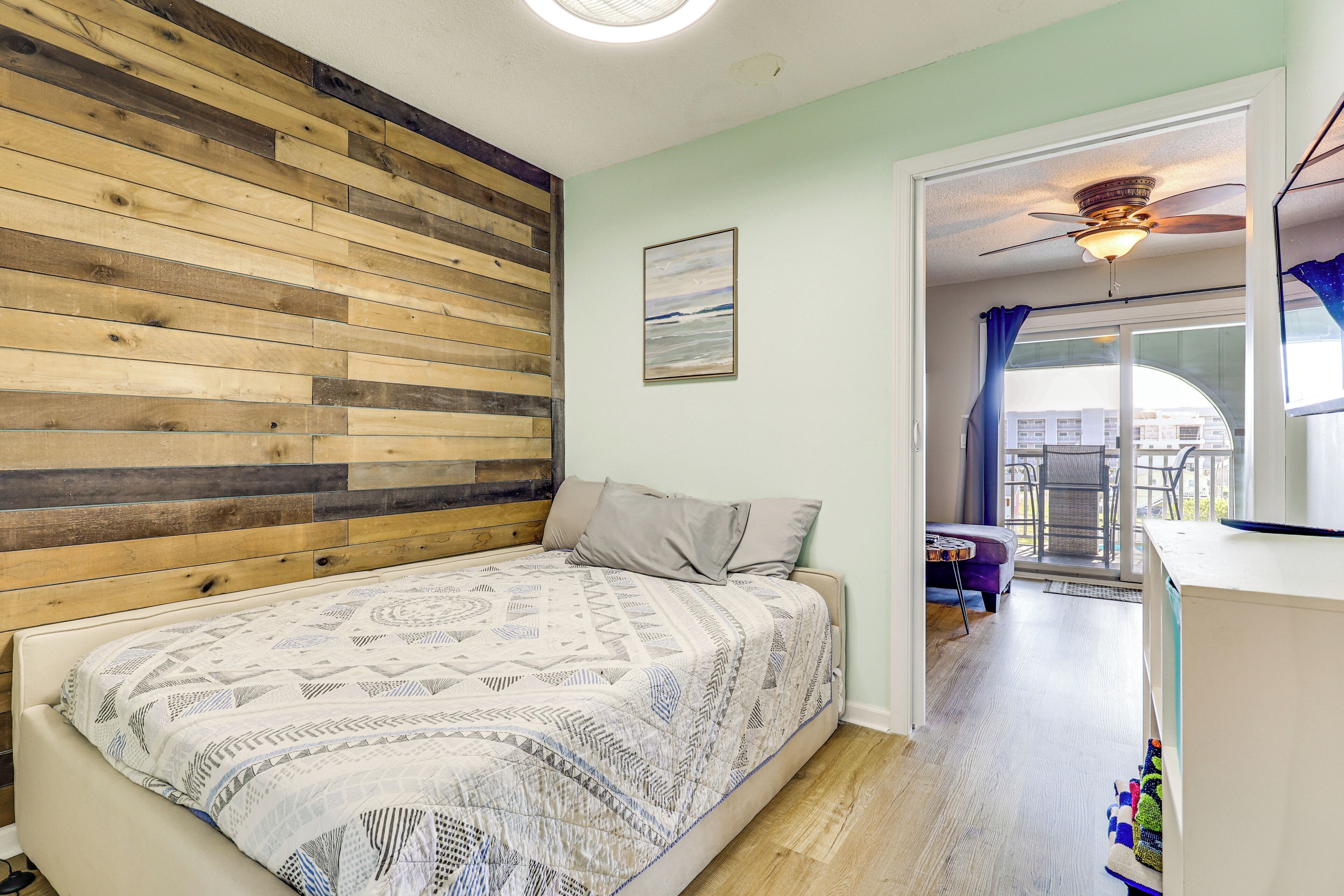 Ein Schlafzimmer mit Bett, einer Holzwand, einem Deckenventilator und Blick ins Freie.