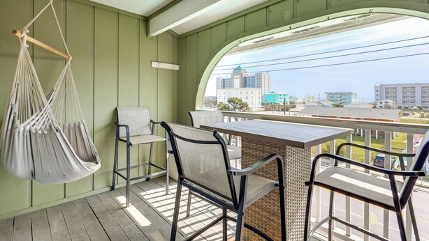 A balcony with a hanging chair, a table, and chairs. - Cozy Carolina Beach Condo w/ Ocean Views! (Carolina Beach)