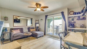 A living room with a sofa, ottoman, coffee table, ceiling fan, and a dining area with a table and chairs. - Cozy Carolina Beach Condo w/ Ocean Views! (Carolina Beach)