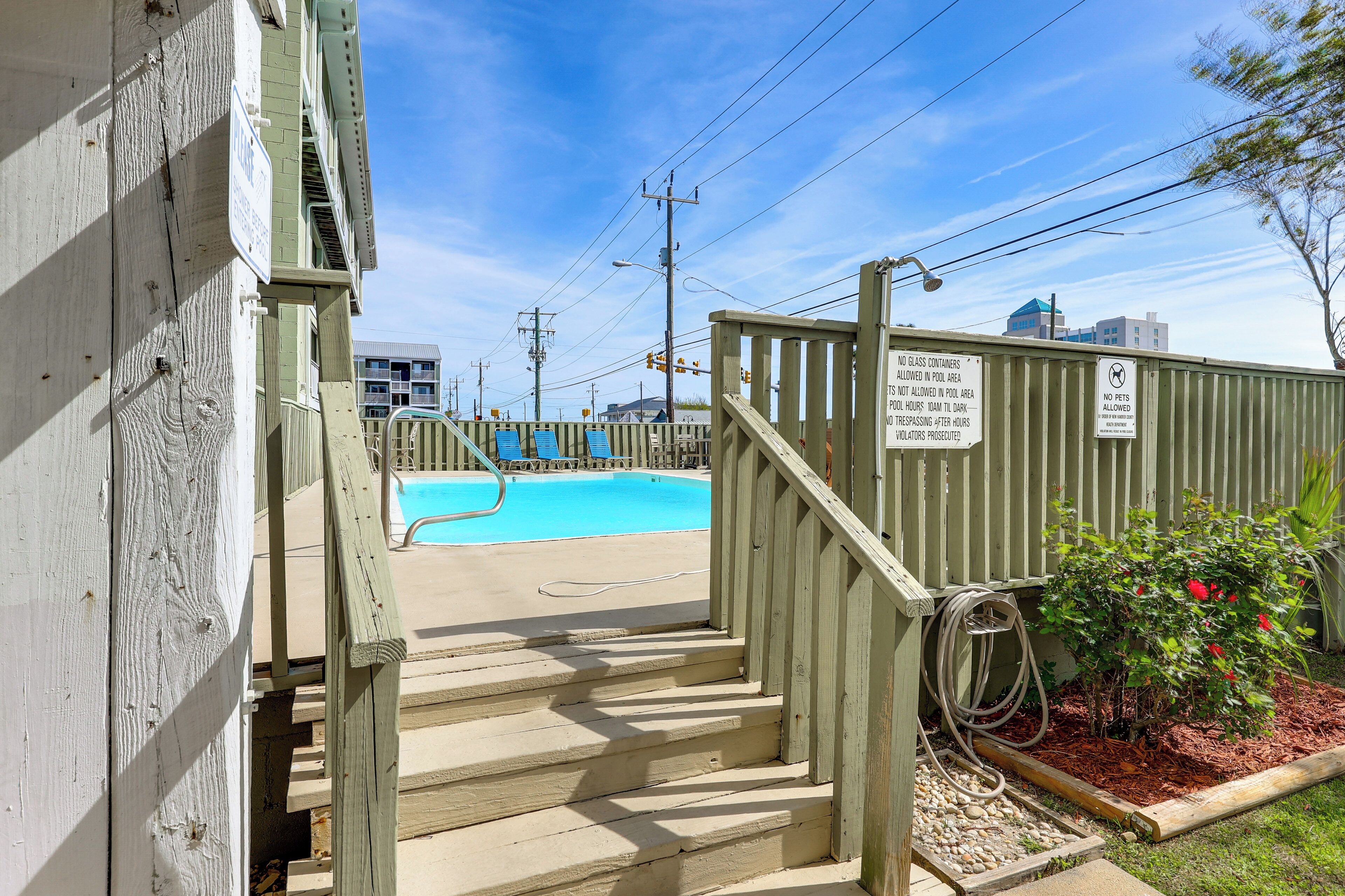 A wooden staircase leading to a pool area with a clear blue sky and a sign prohibiting pets.