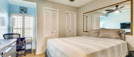 A bedroom with a bed, a desk, a chair, a ceiling fan, and a large mirror.